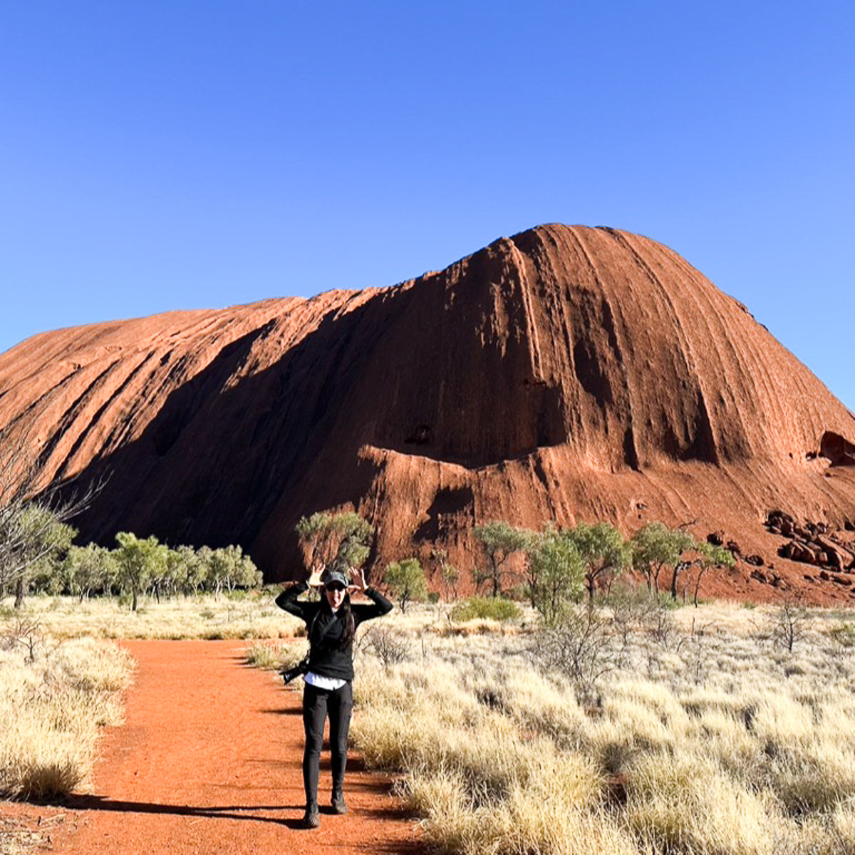 Woman is hiking at ULURU in Australia and is waving at viewer